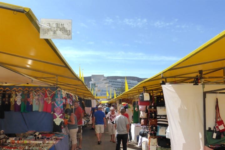 Tourist market in Tenerife with stalls selling clothes, bags and souvenirs under yellow canopies - Los Cristianos market